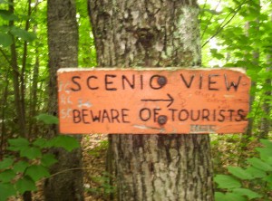 A sign saying "SCENIC VIEW, BEWARE OF TOURISTS"; someone has scrawled "Stupid college kids" on it as well
