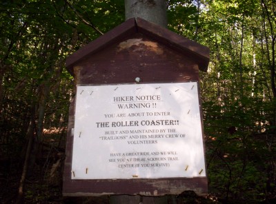 A sign with these words on it: Hiker Notice Warning!  You are about to enter the Roller Coaster!!  Built and maintained by "Trailboss" and his merry crew of volunteers.  Have a great ride and we will see you at the Blackburn Trail Center (if you survive)