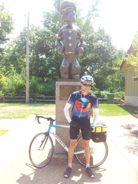 Me striking the flexing-arm-muscles pose in front of a statue of Popeye, with my bike behind; the bike has two rear panniers, and I'm wearing a mostly-hidden Platypus backpack, and that's all the gear I took